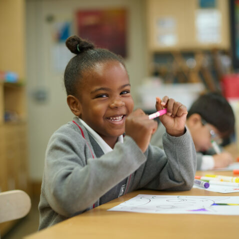 Smiley schoolgirl at her desk with a pink felt tip pen