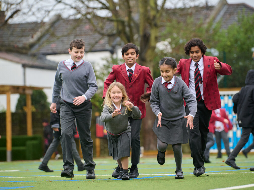 Mixed age group of smiling pupils in grey and maroon uniform, running a race in outdoor playground