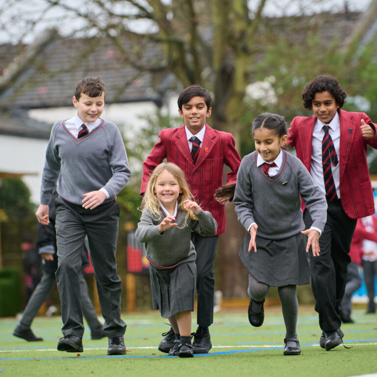 Mixed age group of smiling pupils in grey and maroon uniform, running a race in outdoor playground