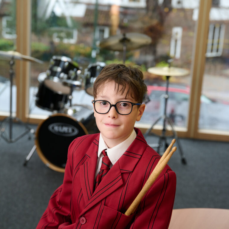 Schoolboy with drumsticks in his pocket. He's sitting in front of a drum kit in The Mall School musicroom