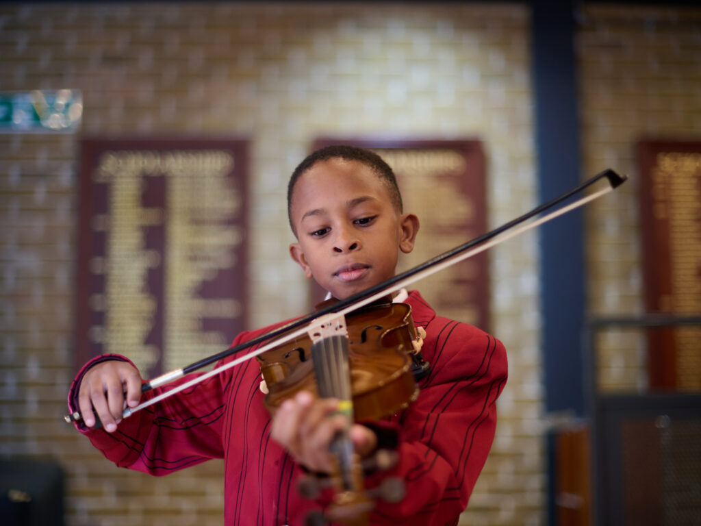 Boy in The Mall School uniform is in the Theatre playing a violin