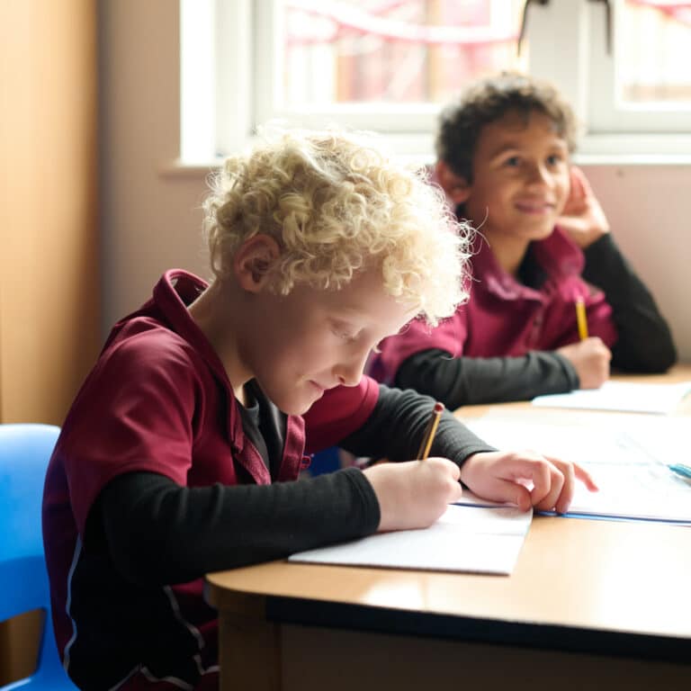 Two boys sitting at their desks, writing in their text books with yellow pencils